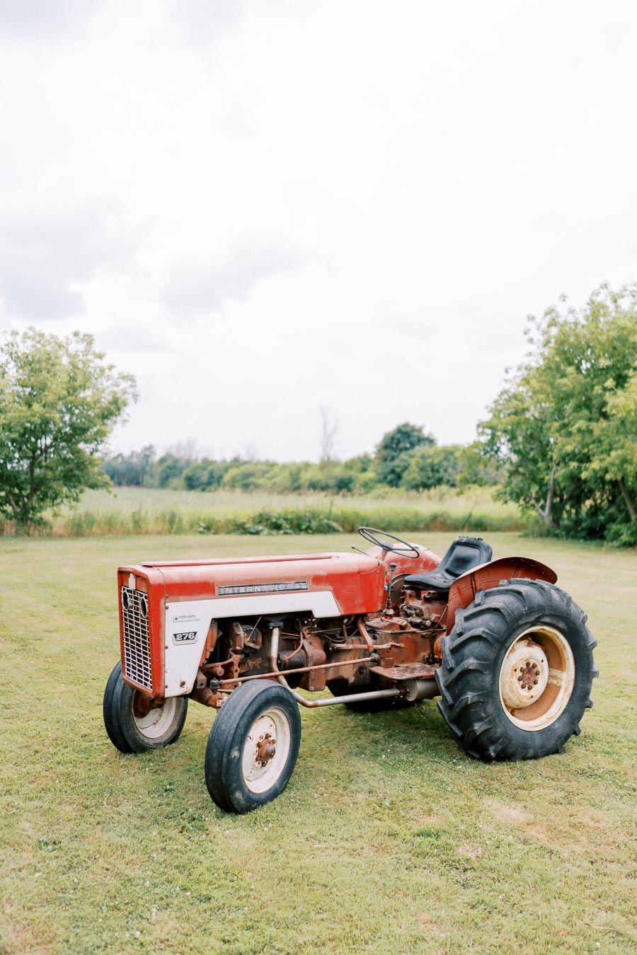 Vintage red tractor on a grassy field with trees in the background, under a cloudy sky.