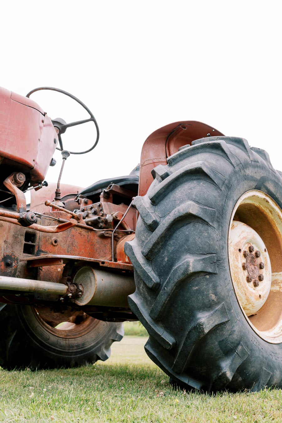 A close-up of a vintage red tractor with large rugged tires on a grassy field, showcasing its rustic and robust design.