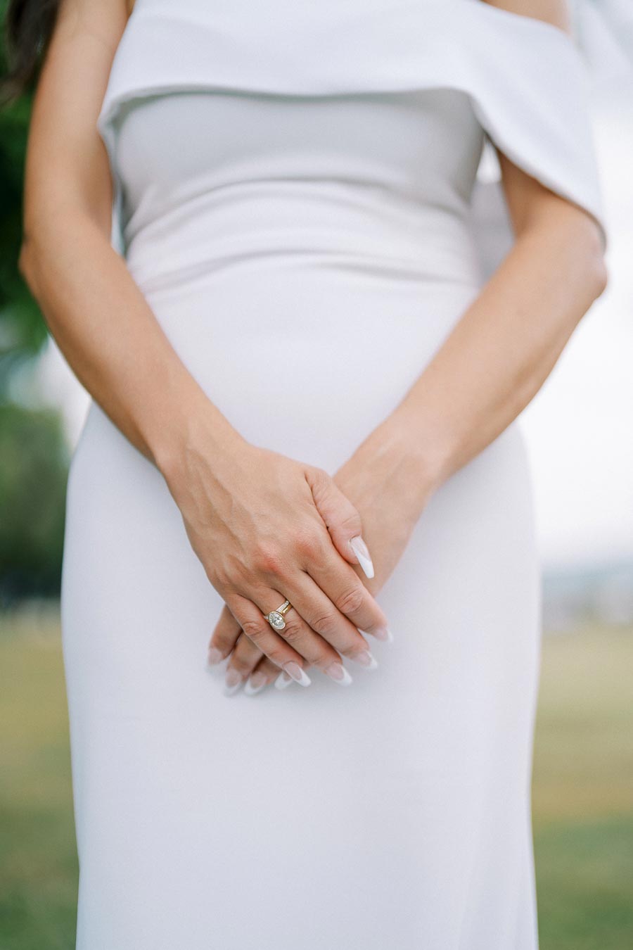 A bride wearing an elegant white gown shows off her engagement ring with neatly manicured nails, symbolizing love and commitment on her wedding day.