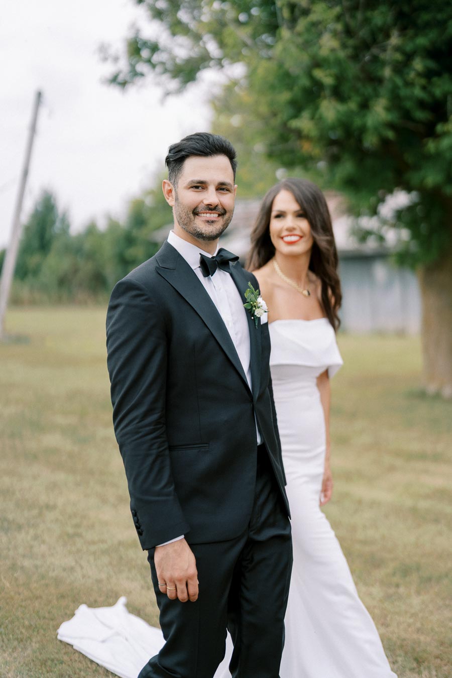 Smiling bride and groom walking outdoors in elegant wedding attire in a lush garden setting