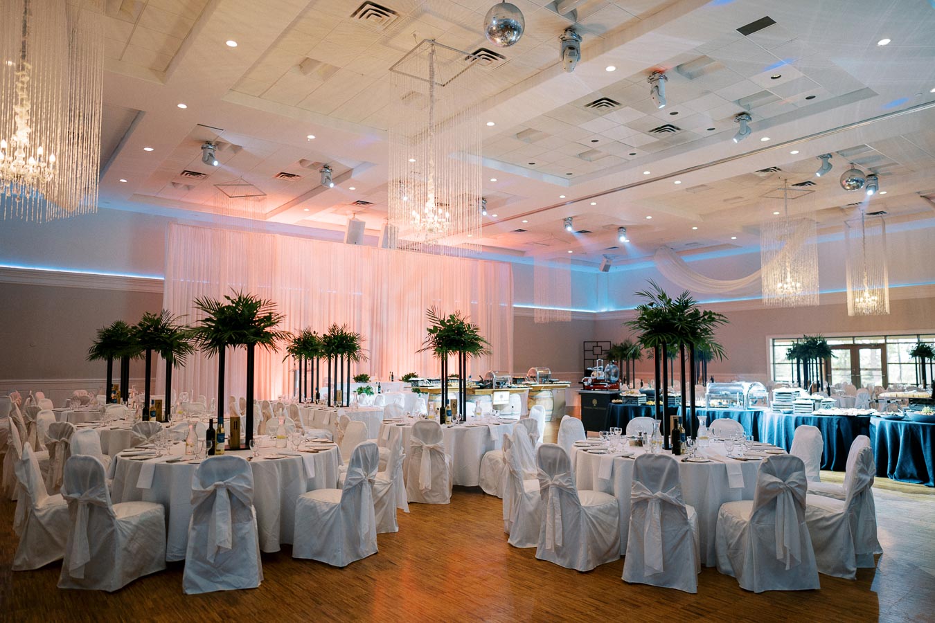 Elegant banquet hall setup with round tables covered in white tablecloths, decorated with tall green centerpieces; ambient lighting creates a warm atmosphere for a sophisticated event.