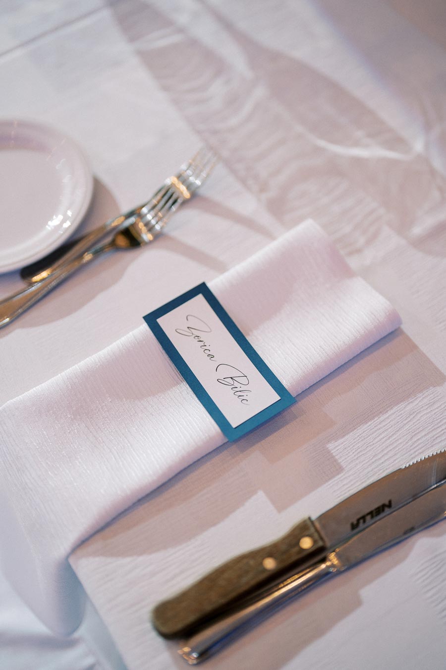 Elegant place setting with a white linen napkin, silver cutlery, and a personalized name card on a dining table.