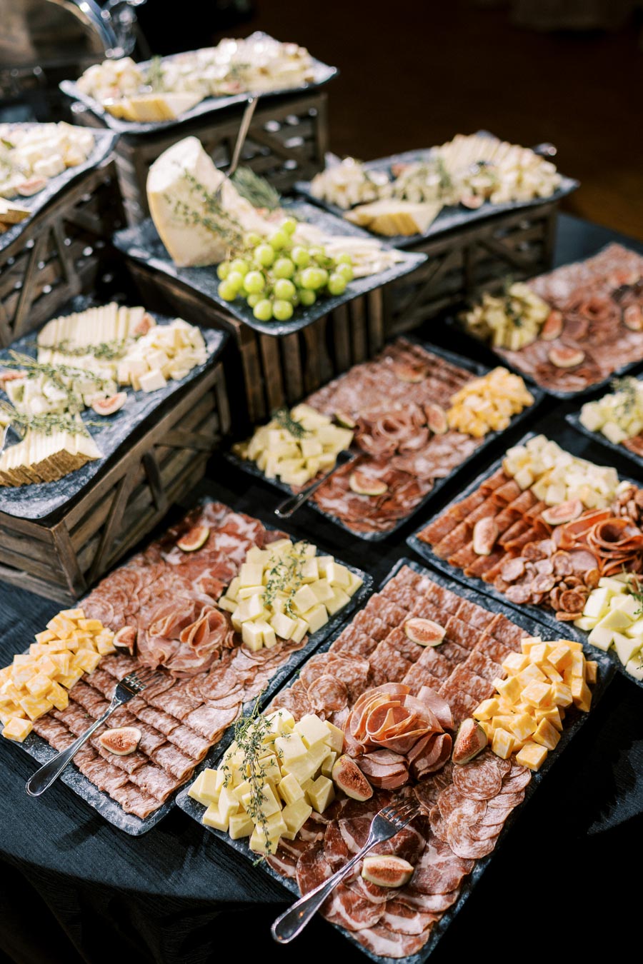 Elegant charcuterie board with an assortment of sliced meats, cheeses, green grapes, and figs, arranged on rustic wooden trays and slate platters for a gourmet presentation.
