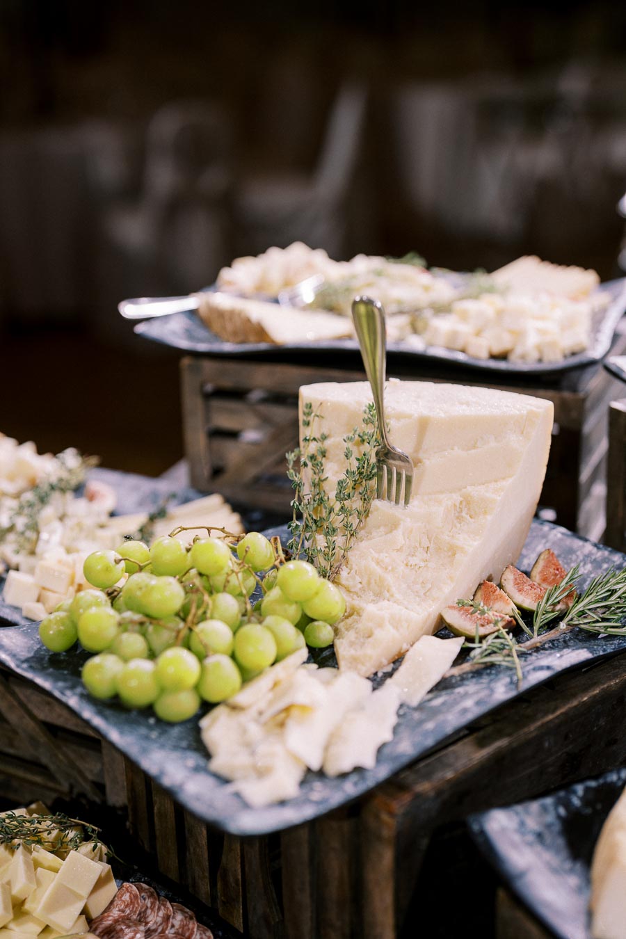 Cheese platter with a large wedge of cheese, clusters of green grapes, sliced figs, and sprigs of rosemary on a slate serving board. Perfect for gourmet gatherings and wine pairings.