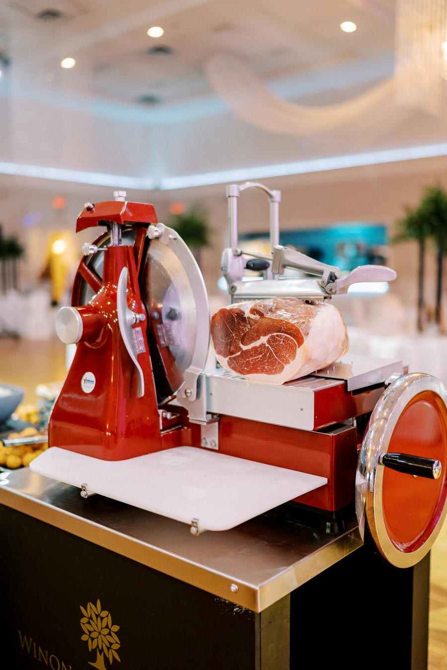 Red vintage meat slicer with a large piece of cured ham on display at a stylish indoor event venue.