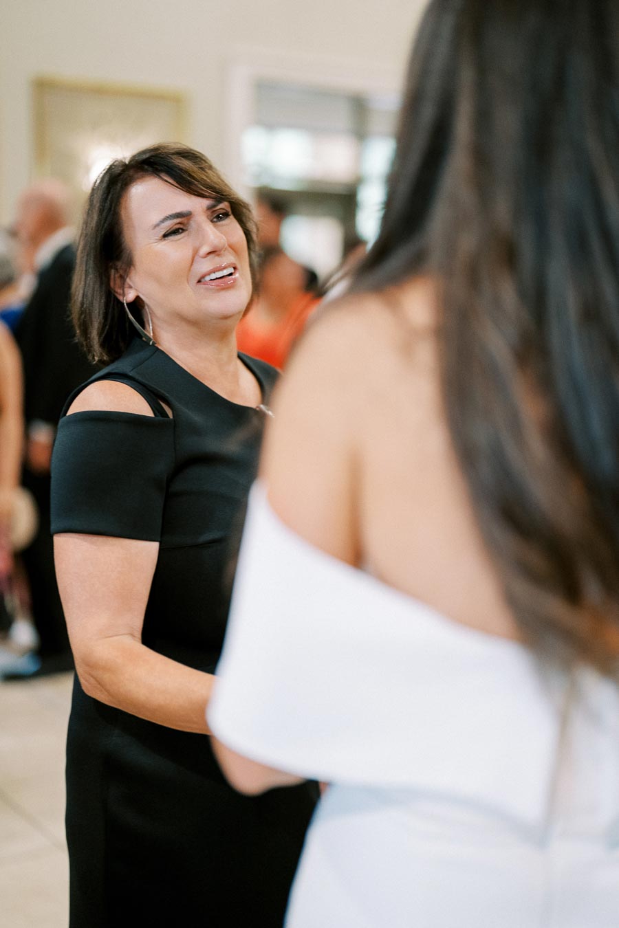 A woman in a black dress smiling and engaging in conversation at a social event.
