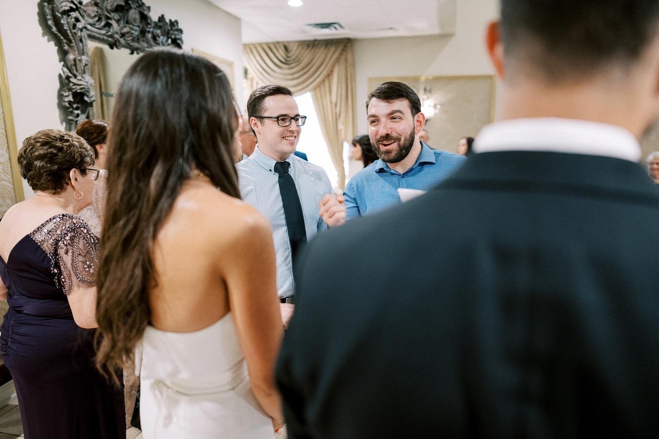 A group of people socializing at an indoor event, with two men engaged in conversation and dressed in formal attire. Other attendees are visible in the background, contributing to a lively and elegant atmosphere.