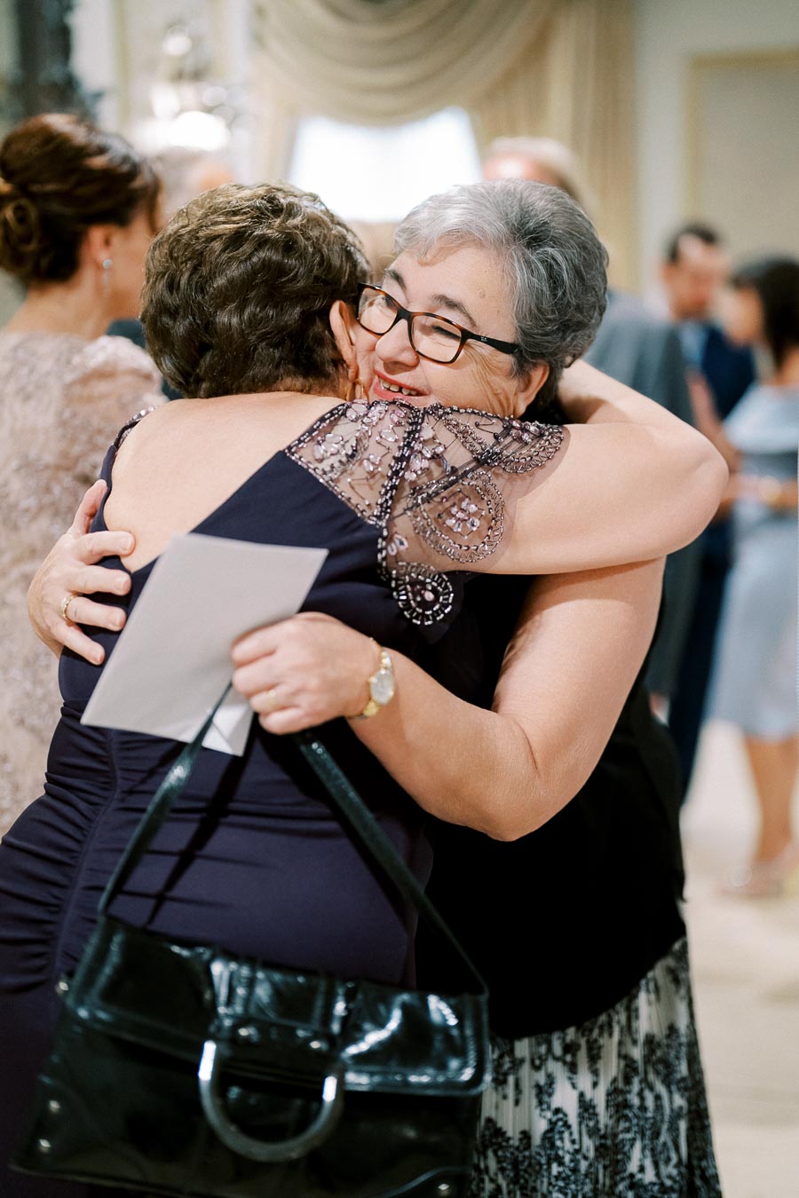 Elderly women embracing warmly at a social gathering, showcasing friendship and affection.