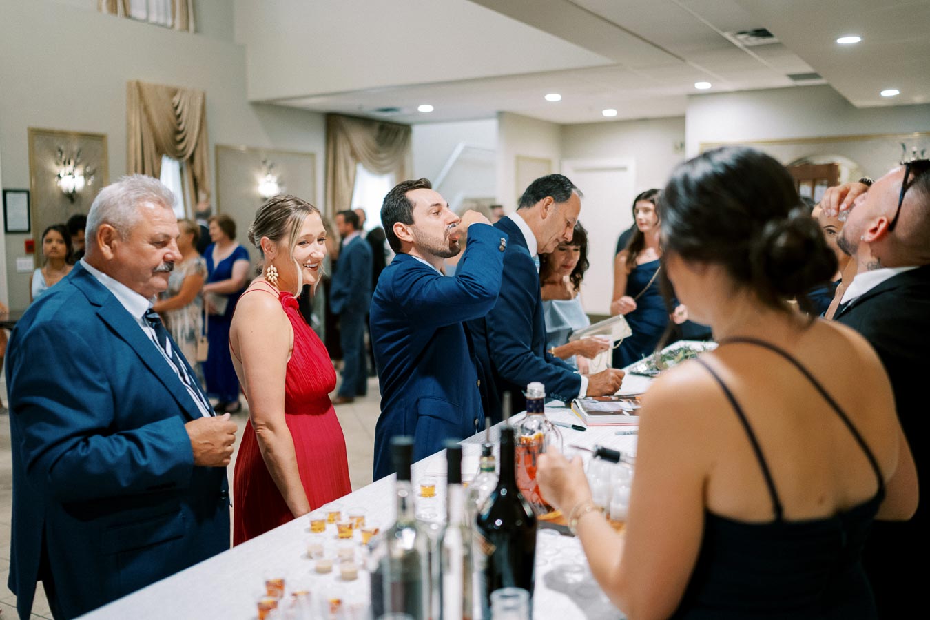 Guests enjoying drinks and socializing at a formal event with a lively atmosphere, featuring elegantly dressed individuals at a bar counter.