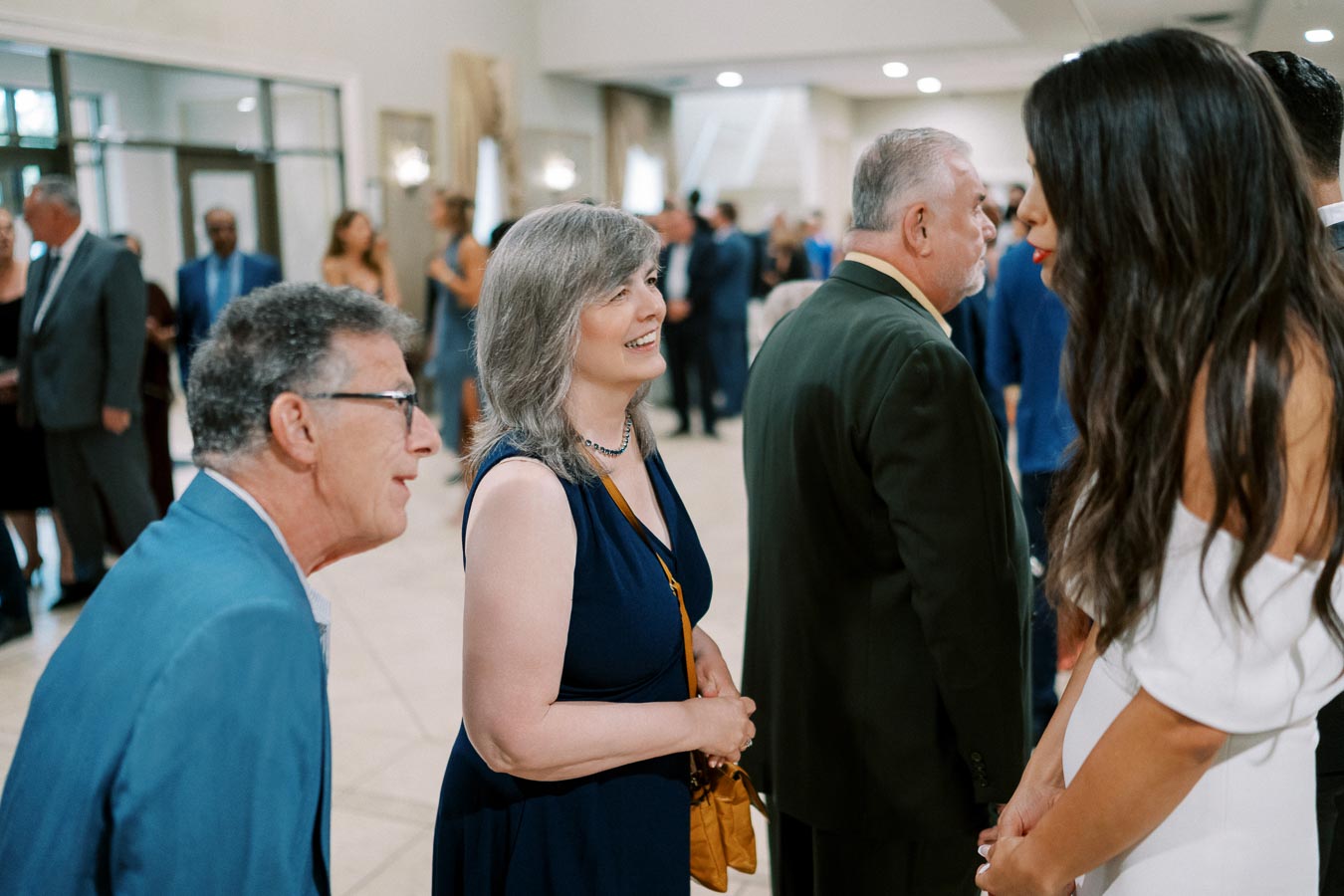A group of people dressed in formal attire, engaging in conversation at a social event indoors.