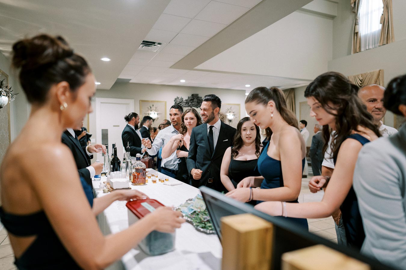 Guests socializing at a formal event bar, with people dressed in elegant attire, conversing and enjoying drinks in a sophisticated atmosphere.