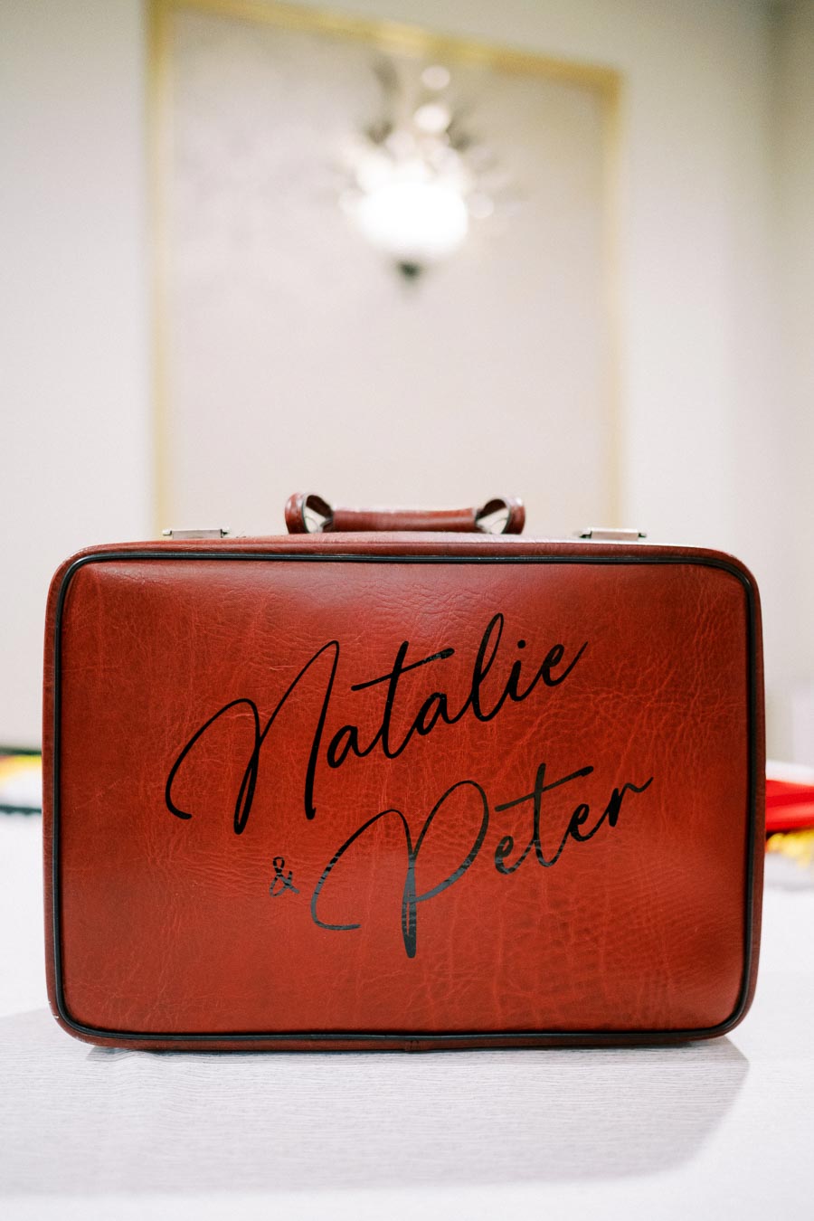 Red suitcase with elegant script text reading Natalie & Peter on a white background, ideal for wedding or travel-themed content.
