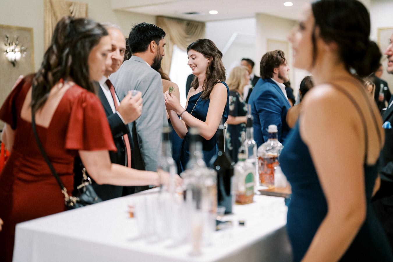 Guests in formal attire enjoy socializing and drinks at an elegant event reception, featuring a well-stocked bar and a lively atmosphere.