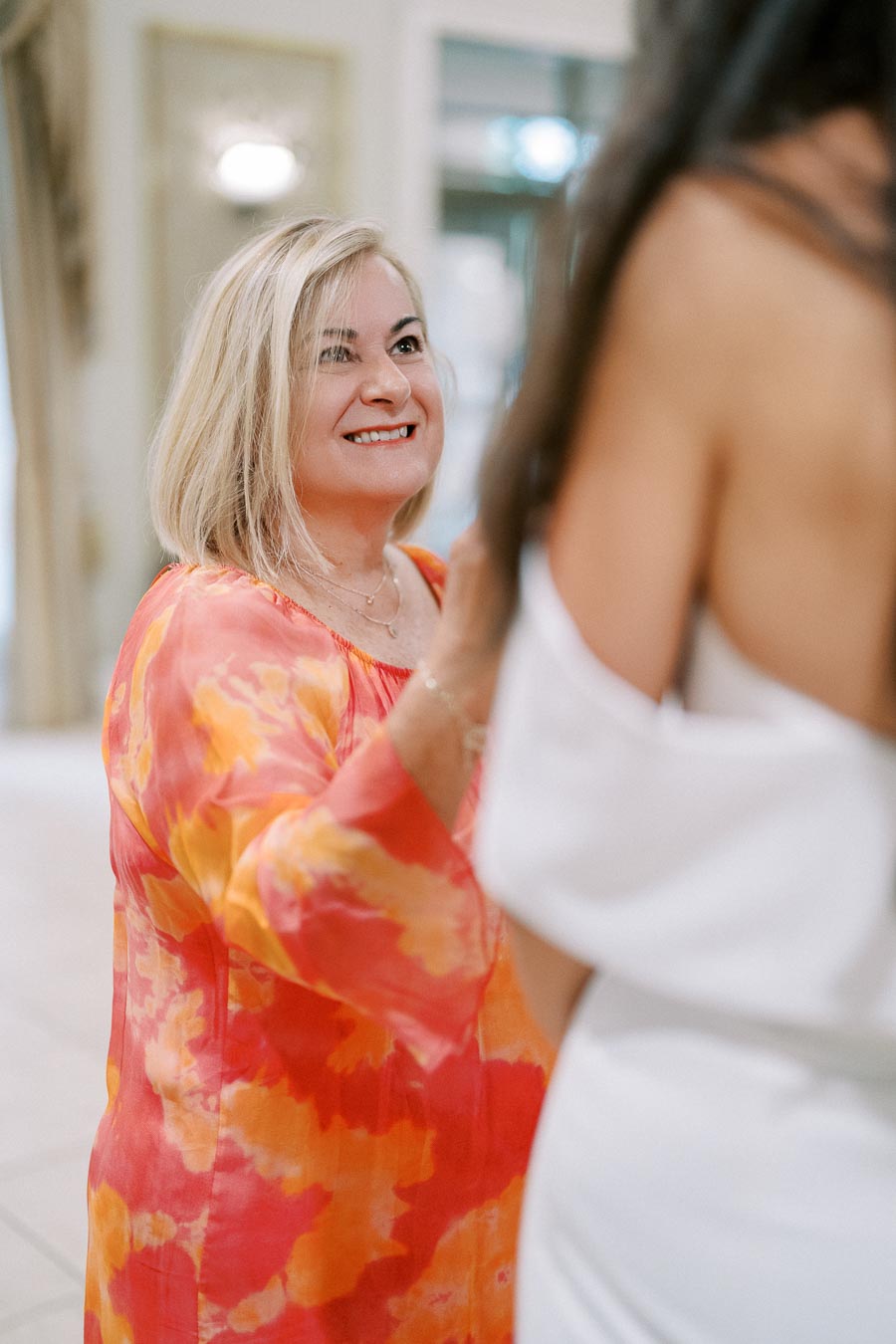 A woman in a colorful orange and pink dress interacting with another person at an indoor event, smiling and engaged.