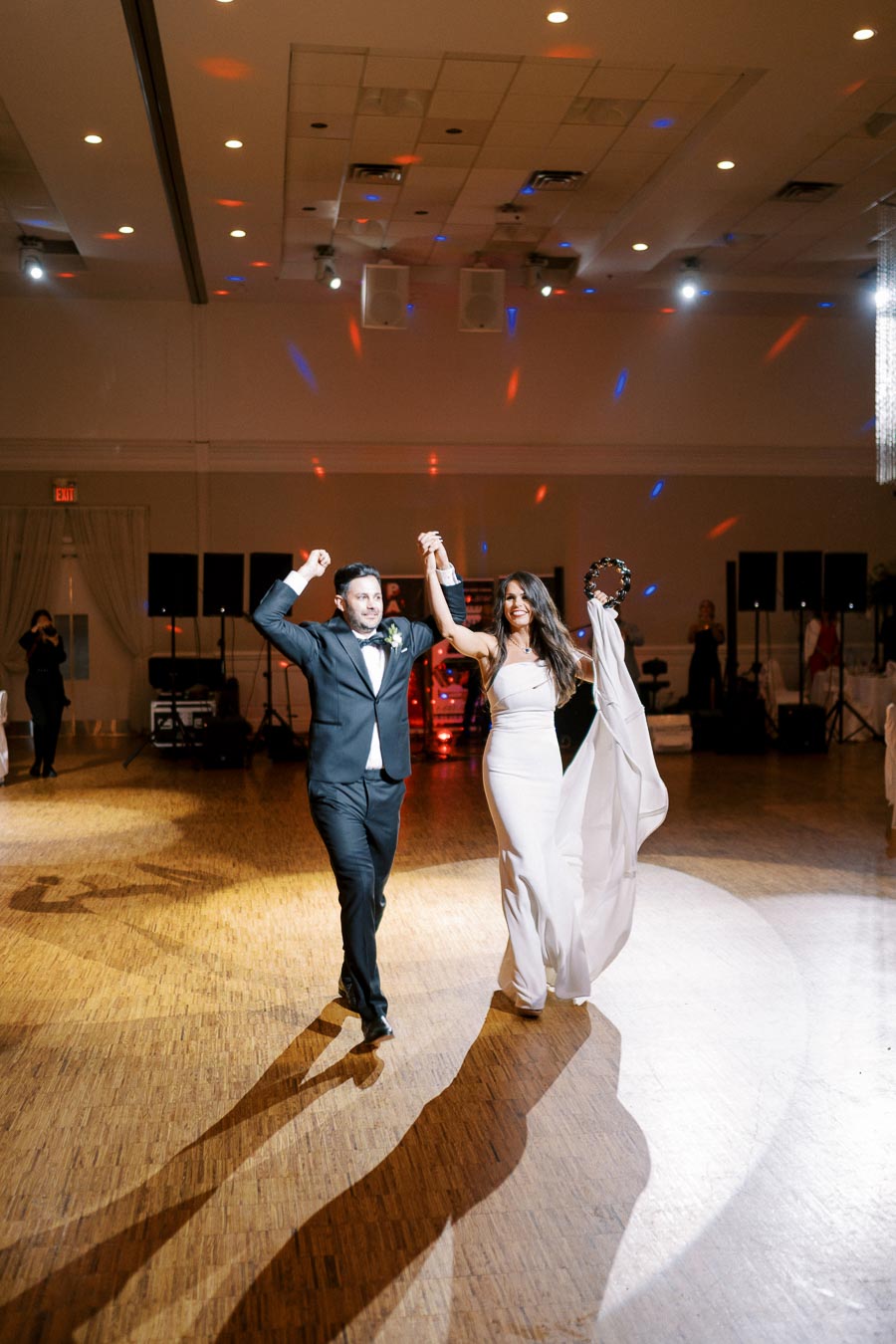 A joyful bride and groom celebrating on the dance floor at their wedding reception with elegant lighting and decor.