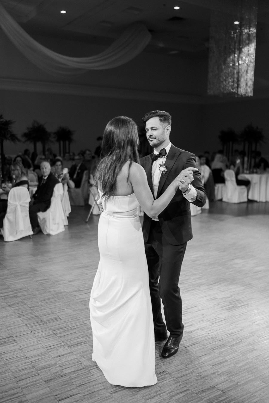 Black and white image of a couple dancing elegantly at a formal event, surrounded by seated guests.
