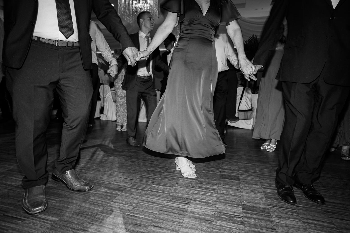 Black and white image of people dancing in formal attire at an elegant indoor event, showcasing movement and celebration on a wooden dance floor.