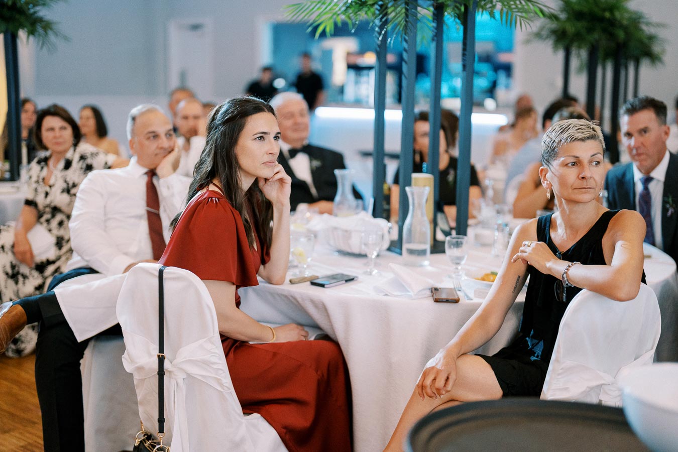 A group of people seated around elegantly decorated tables at a formal event, attentively listening to a presentation.