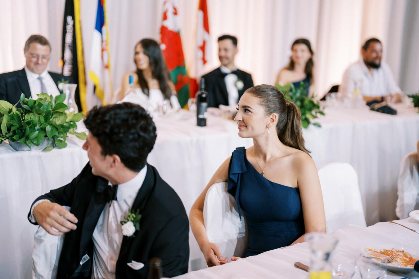 Guests at a formal event sitting at a decorated table with flags and elegant place settings, highlighting a sophisticated ambiance.
