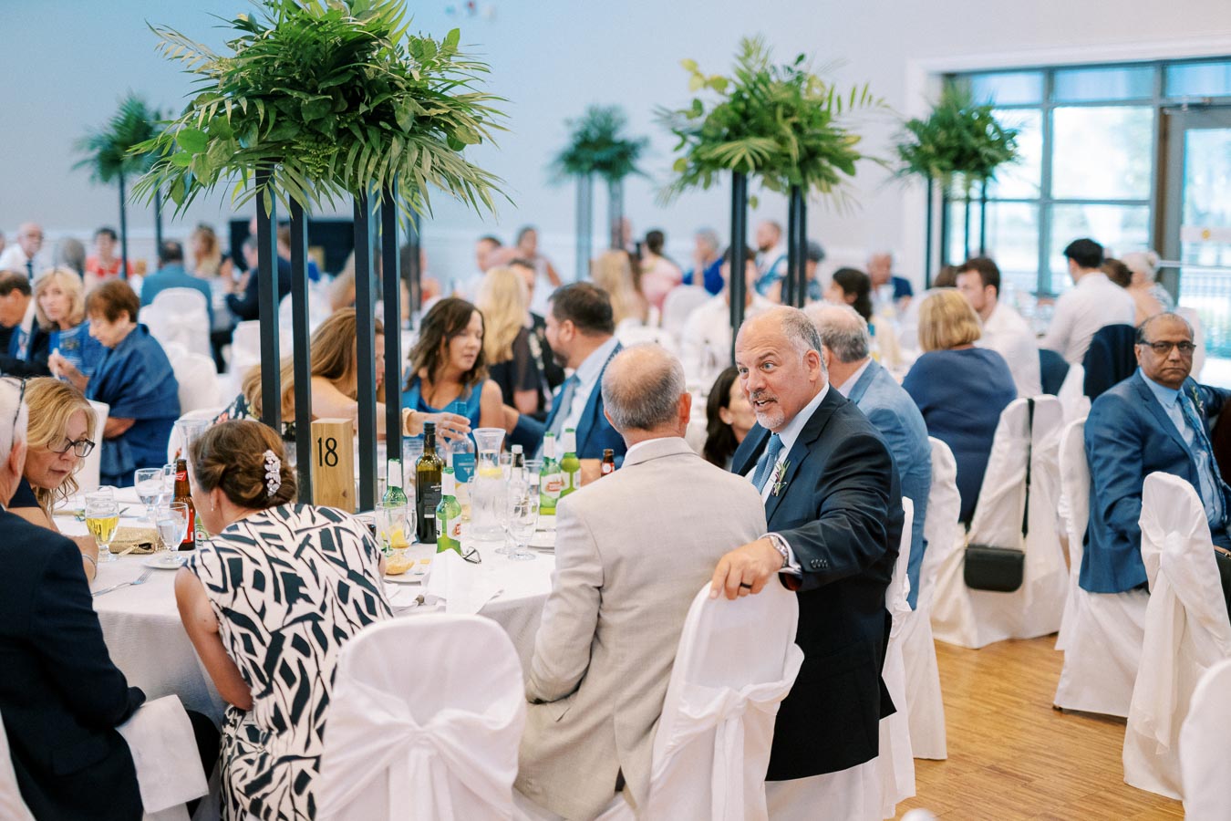 Guests seated at elegantly decorated tables with white linens and green floral centerpieces during a formal event in a bright, spacious venue.