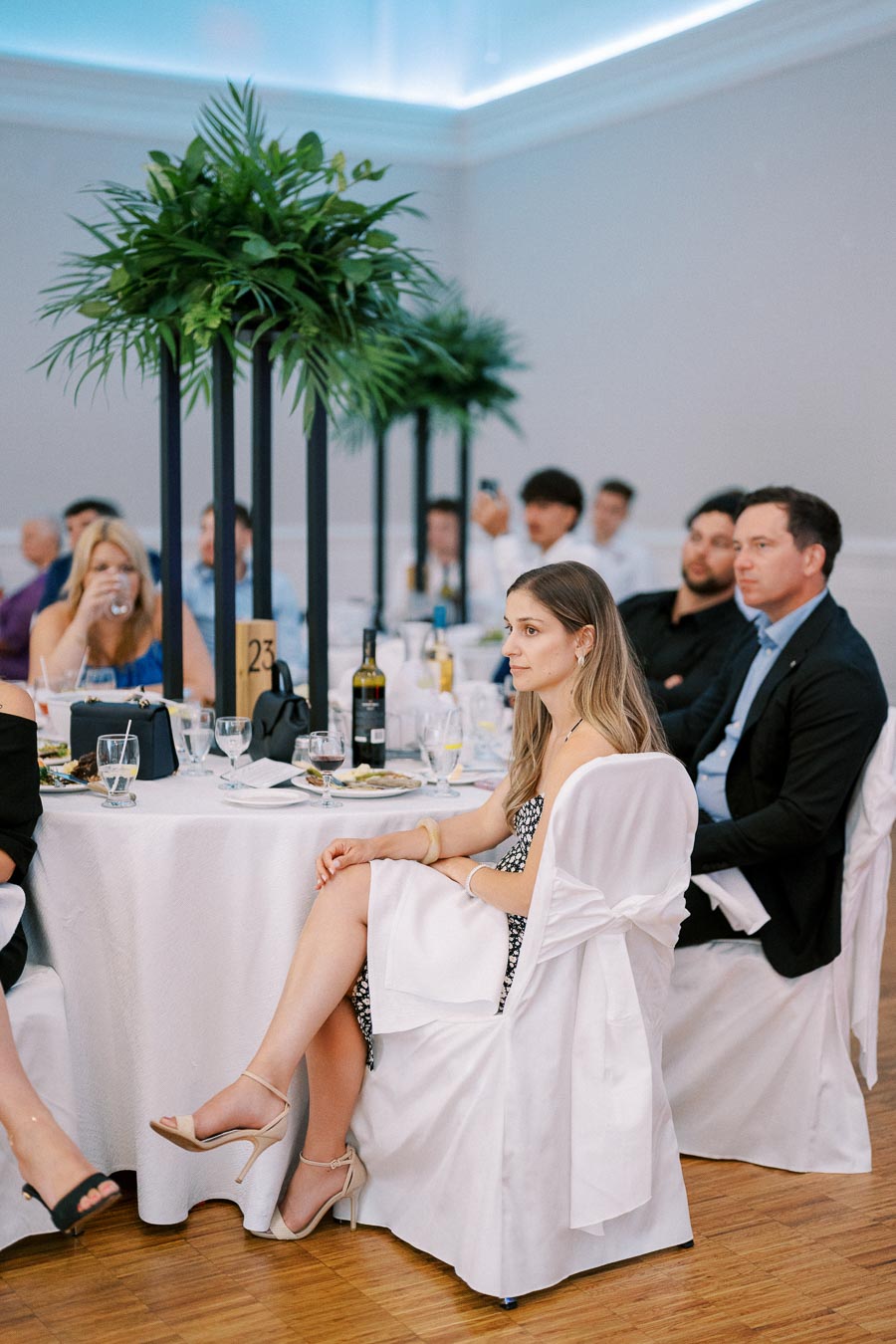 Guests seated at an elegantly decorated table with white linens and tall floral centerpieces during a formal event or wedding reception.