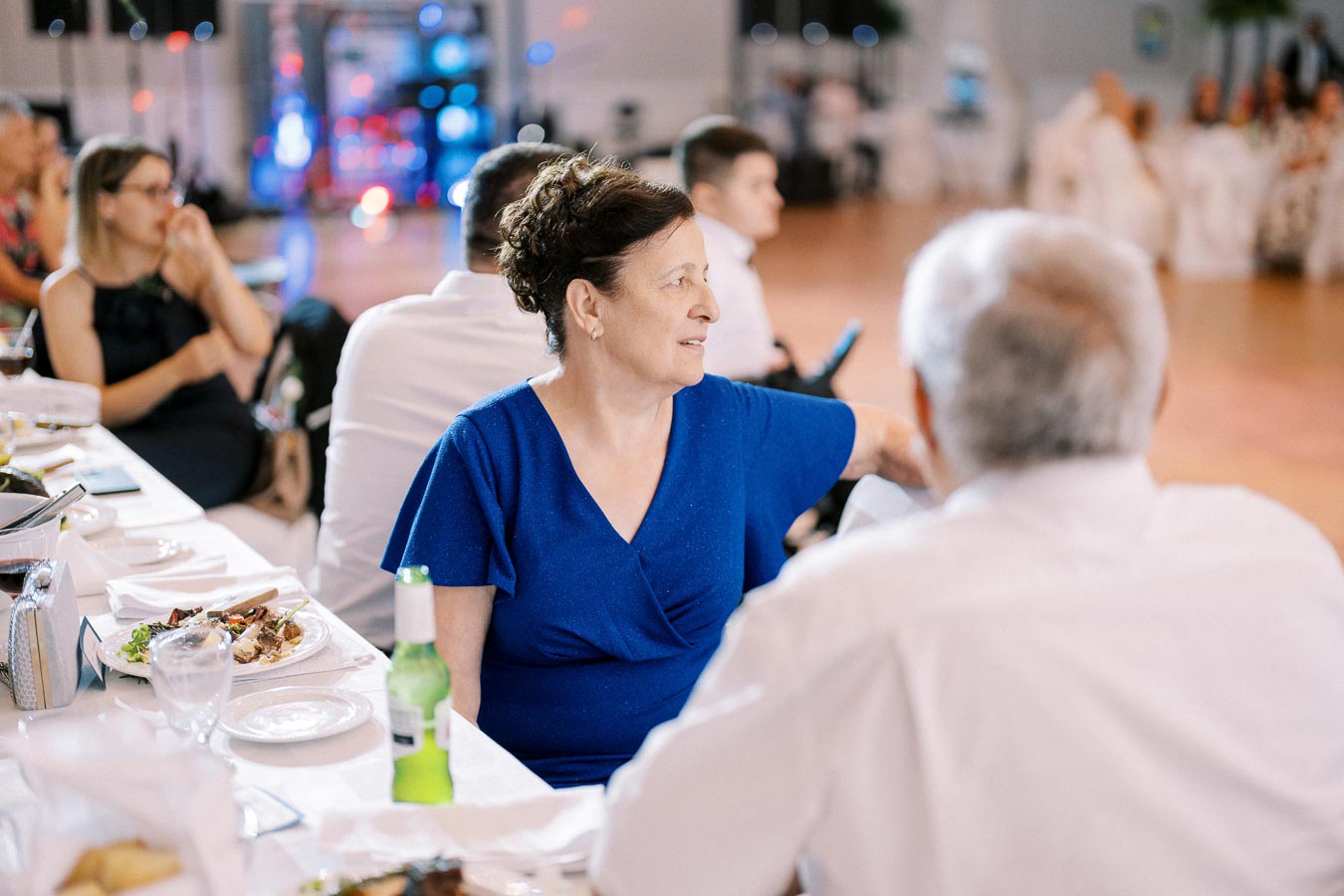 Elegant woman in blue dress attending a formal event, seated at a dining table with others in a banquet hall setting.