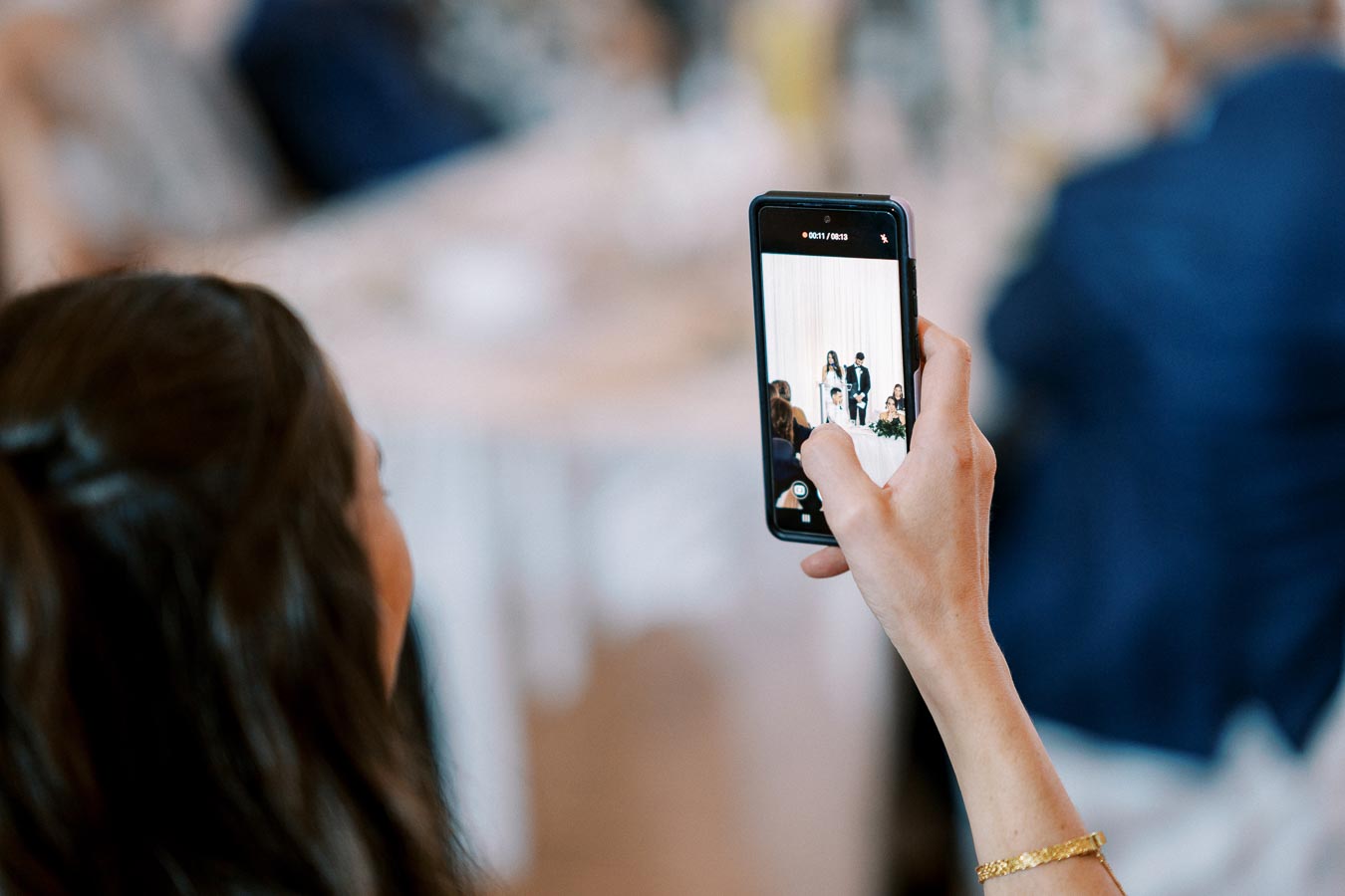 A person taking a photo with a smartphone at a wedding ceremony, capturing the couple at the altar.