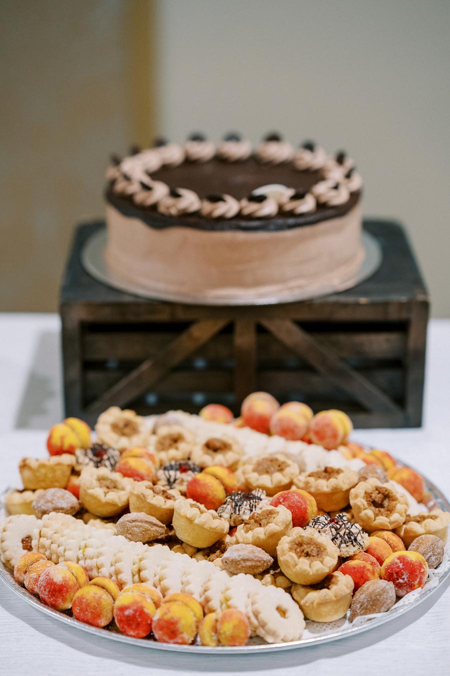A delicious display of desserts featuring a chocolate frosted cake on a wooden stand and an assortment of cookies and pastries on a silver platter.