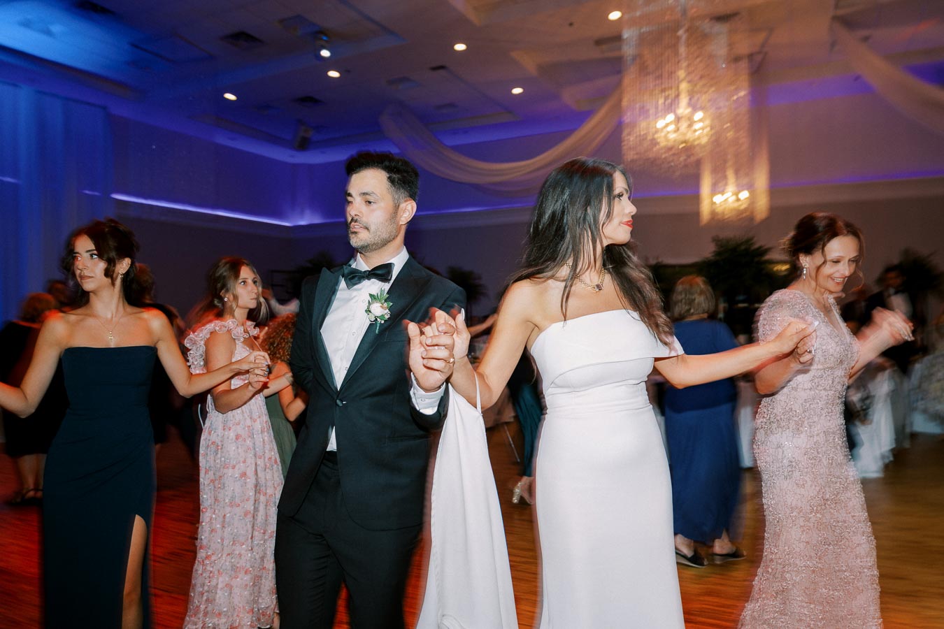 A group of elegantly dressed people dancing at a formal event with a beautifully lit ceiling and chandelier in the background.