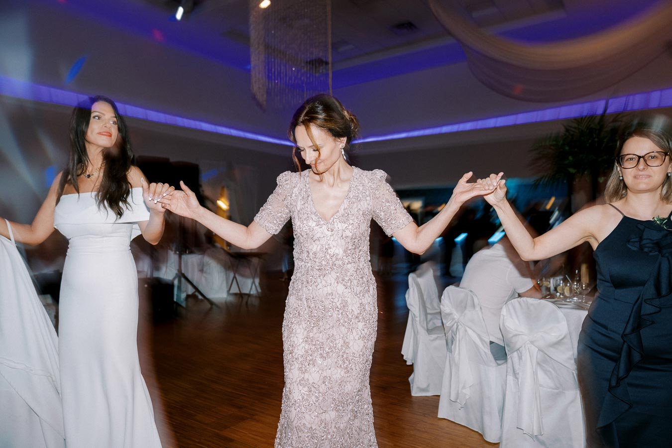 Three elegantly dressed women dancing joyfully at an indoor celebration.