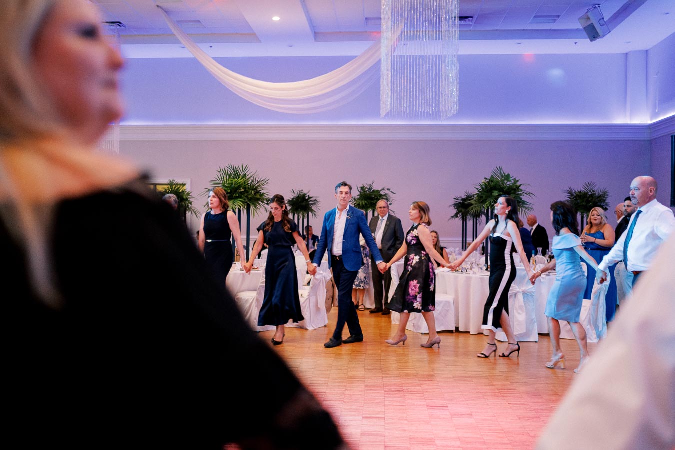 Guests enjoying a lively dance at an elegant indoor wedding reception, surrounded by stylish decor and soft lighting.