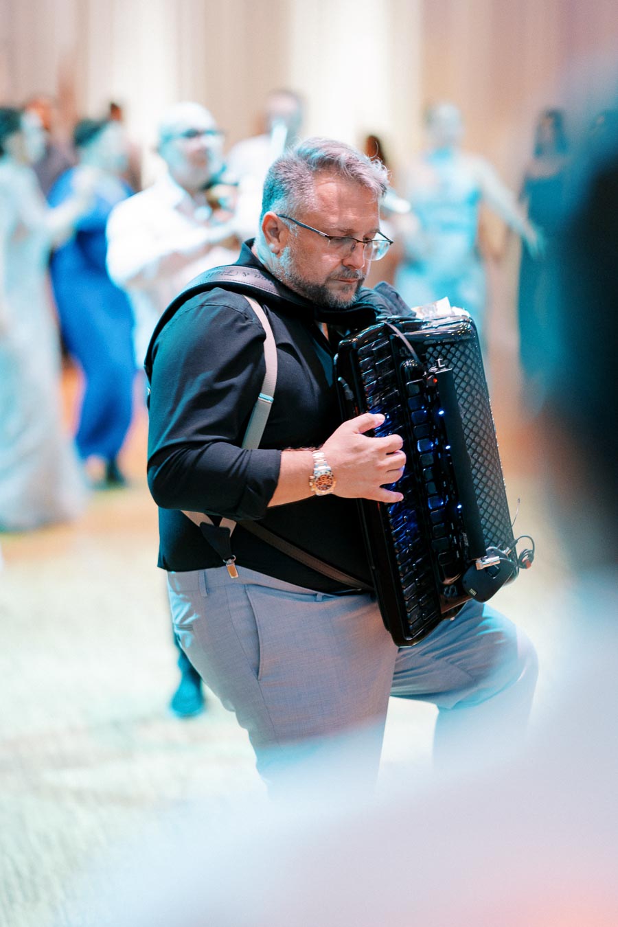 Man playing accordion at an event with blurred attendees in the background, creating a lively atmosphere.