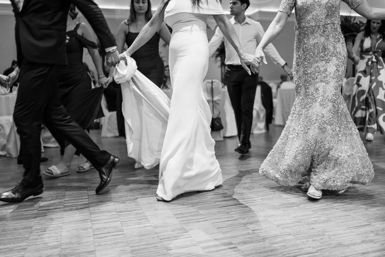 Black and white photo of elegantly dressed people dancing at a formal event, showcasing a lively celebration atmosphere with a focus on movement and fashion.