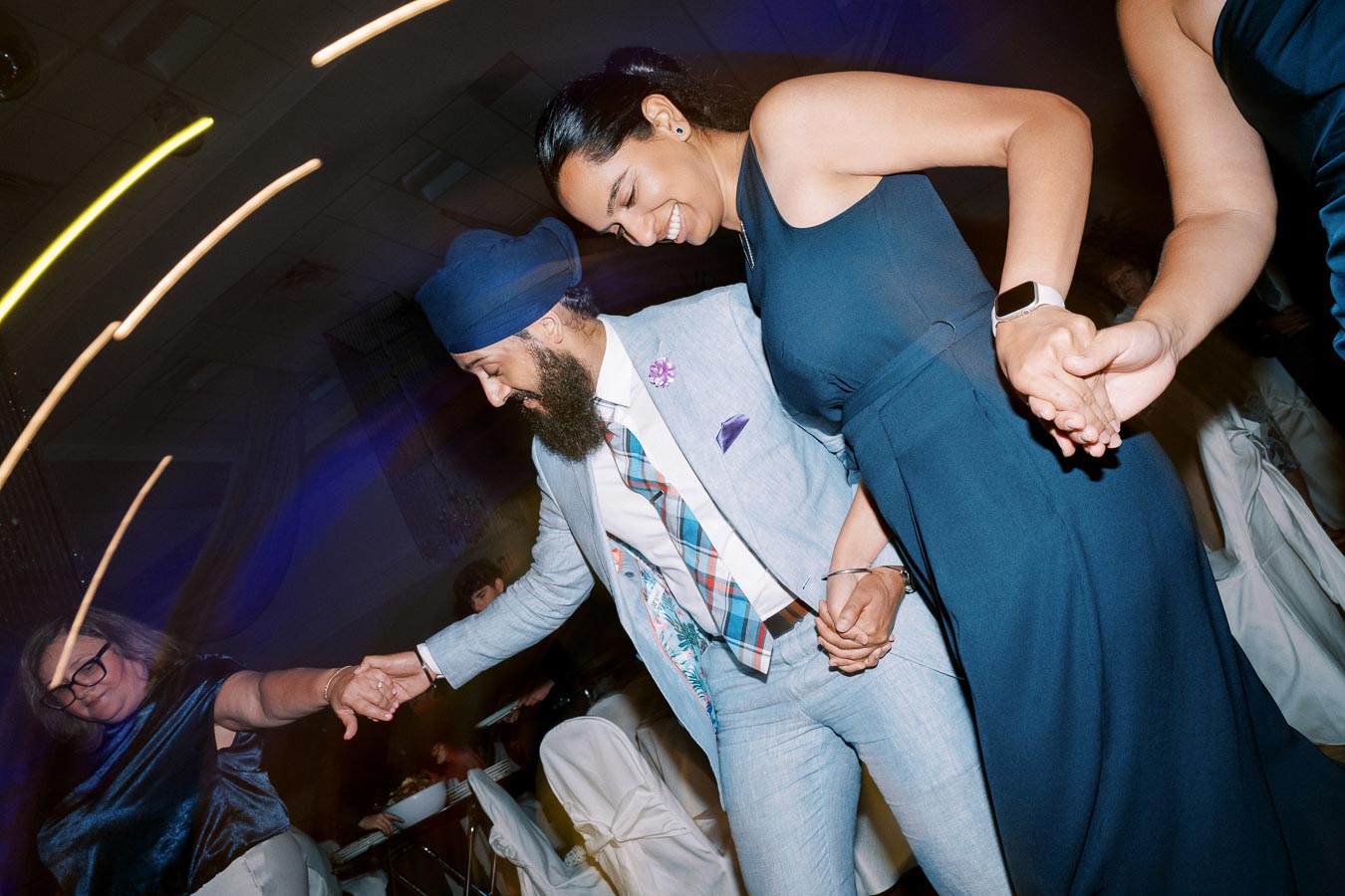A group of people joyfully dancing together at a lively indoor event, with colorful lights creating a festive atmosphere.