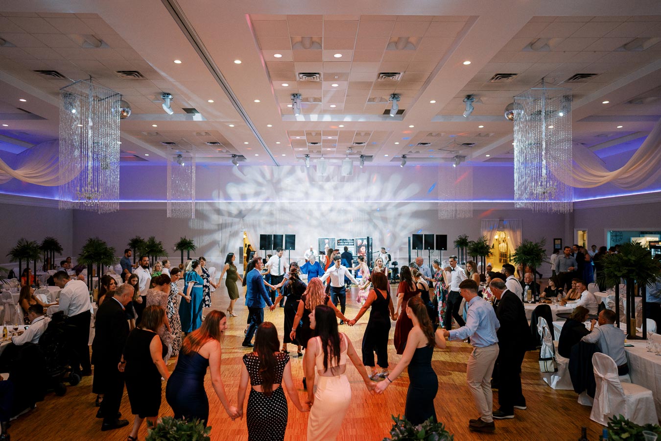 Wedding reception dance floor with guests forming a circle under elegant lighting and decor.