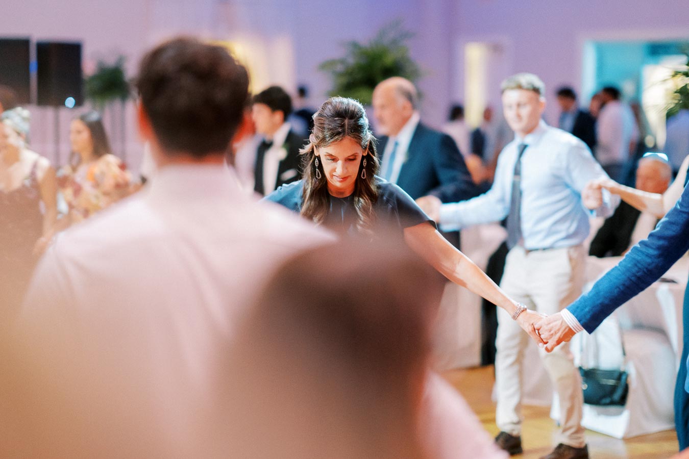 A group of people holding hands and dancing at a lively indoor event with blurred background.