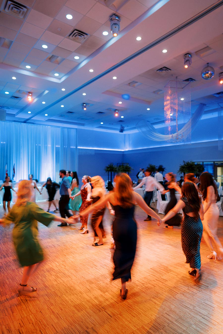 A lively group of people dancing in a circle at a vibrant indoor event with colorful lighting, capturing a festive and joyful atmosphere.
