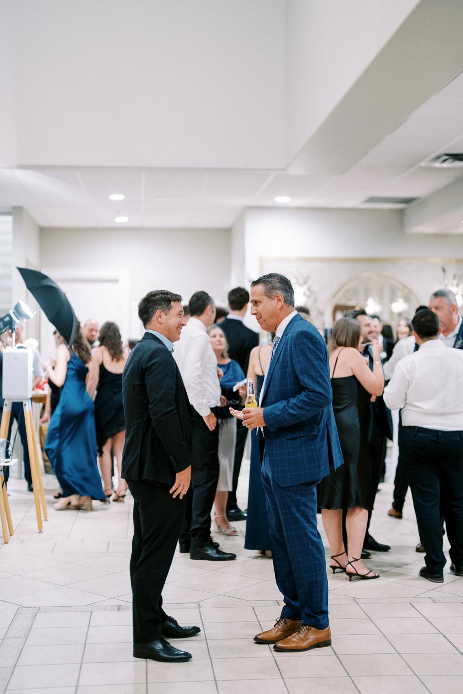 A lively indoor social gathering with people dressed in formal attire, engaging in conversations and enjoying drinks, creating a vibrant and elegant event atmosphere.