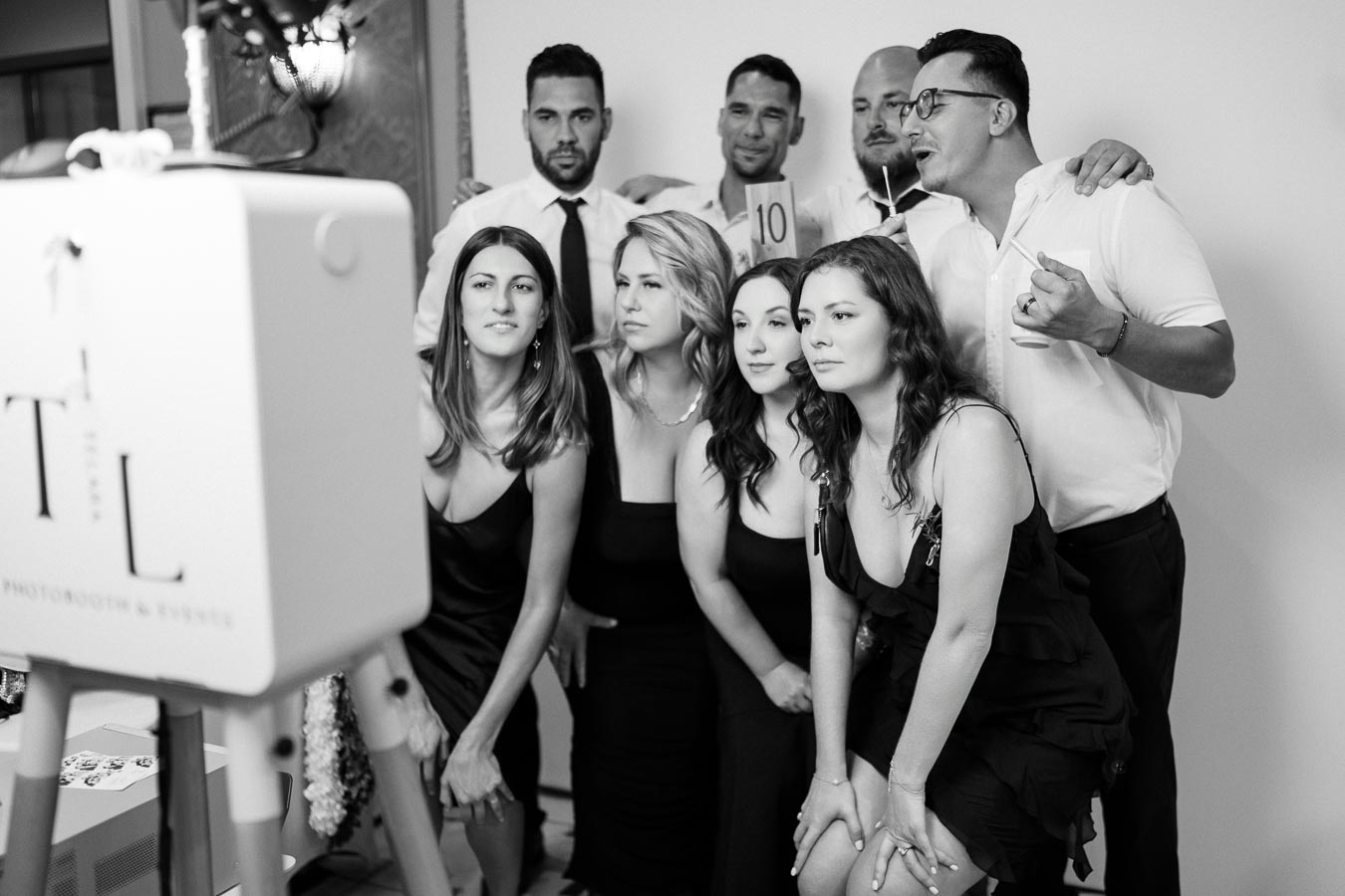 A group of people in formal attire posing for a photo booth at an event, with a camera setup in the foreground.