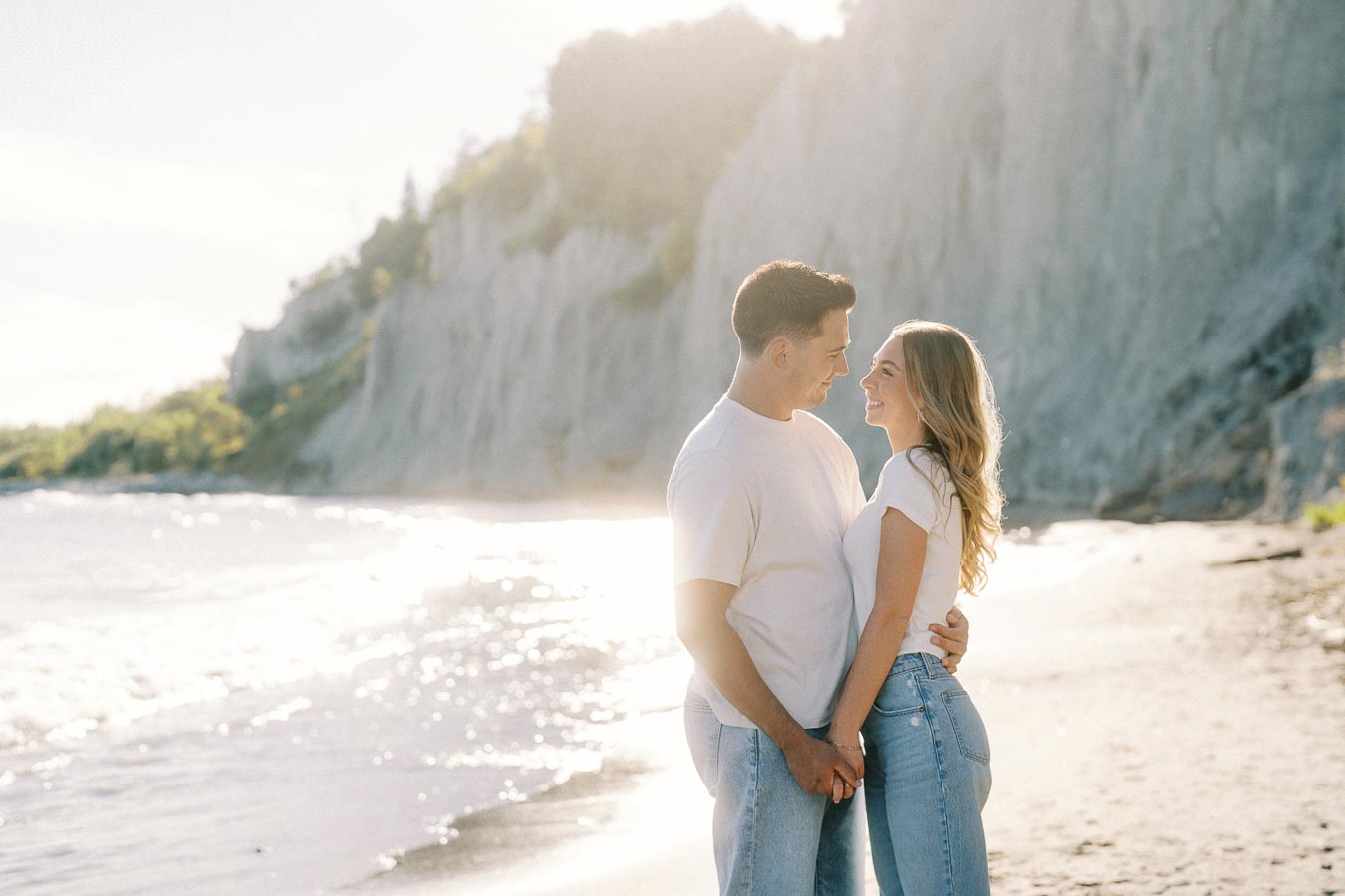 Couple embracing on a sunny beach with cliffs in the background, showcasing love and romance on a scenic coastline.
