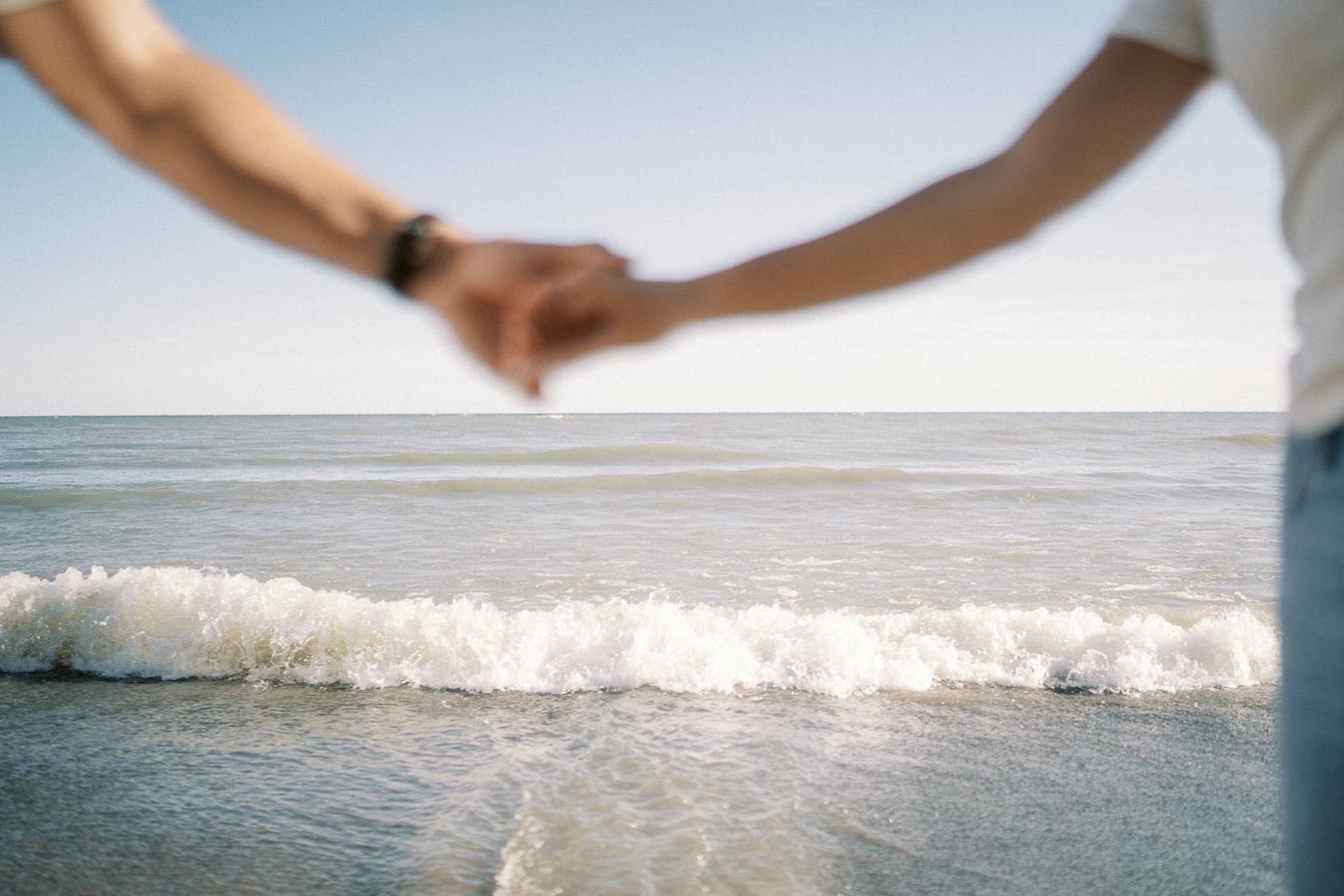 Couple holding hands at the beach with waves in the background, symbolizing romantic seaside getaway or beachside romance.