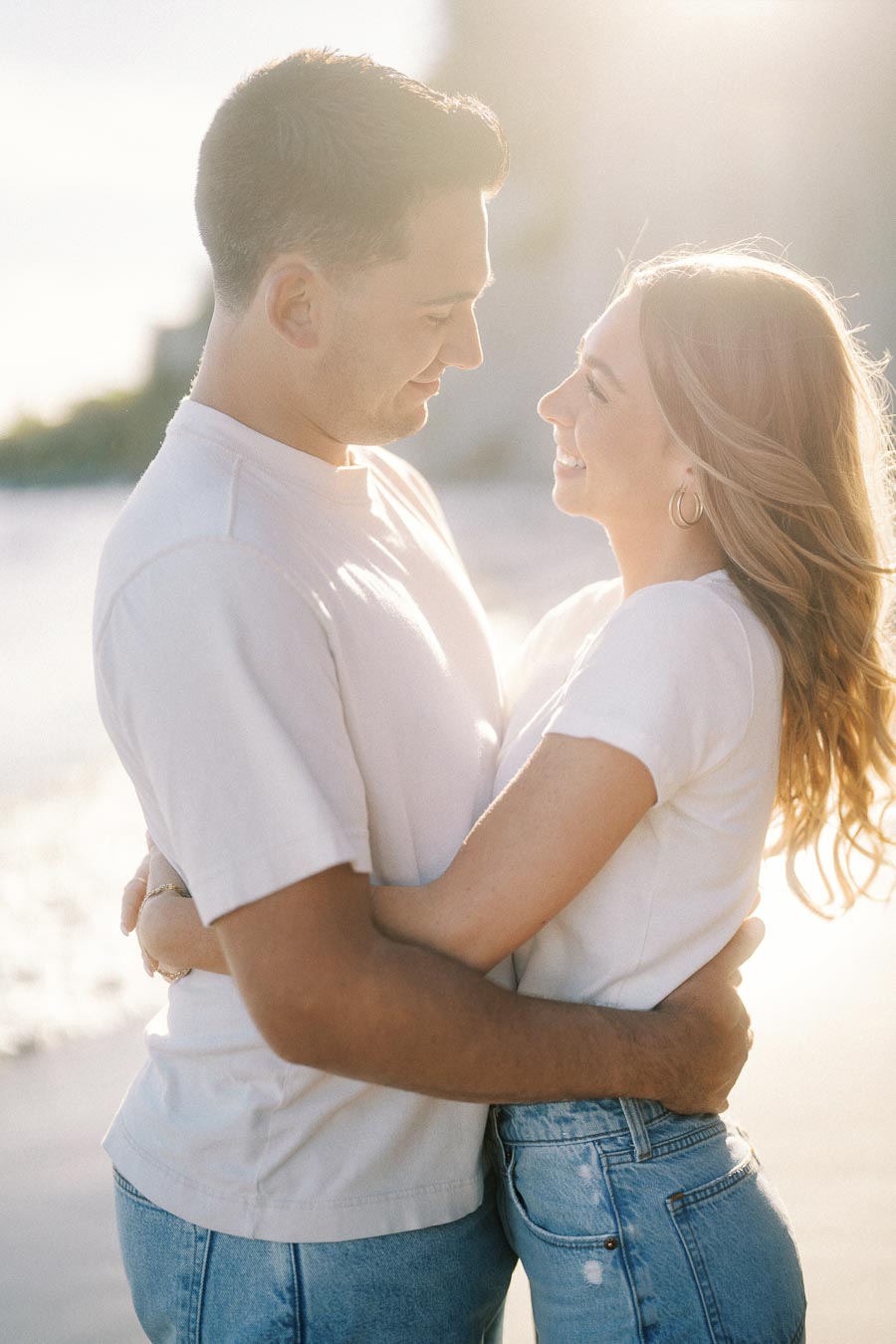 Couple Embracing on a Sunlit Beach, Smiling and Enjoying a Romantic Moment Together