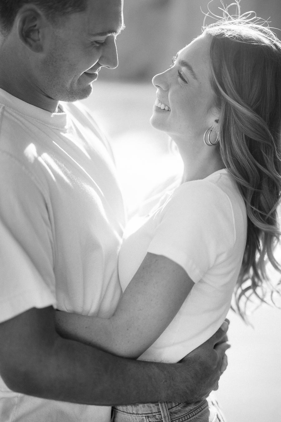A couple embracing and smiling at each other in a black and white photo, wearing casual outfits, representing joy and affection.