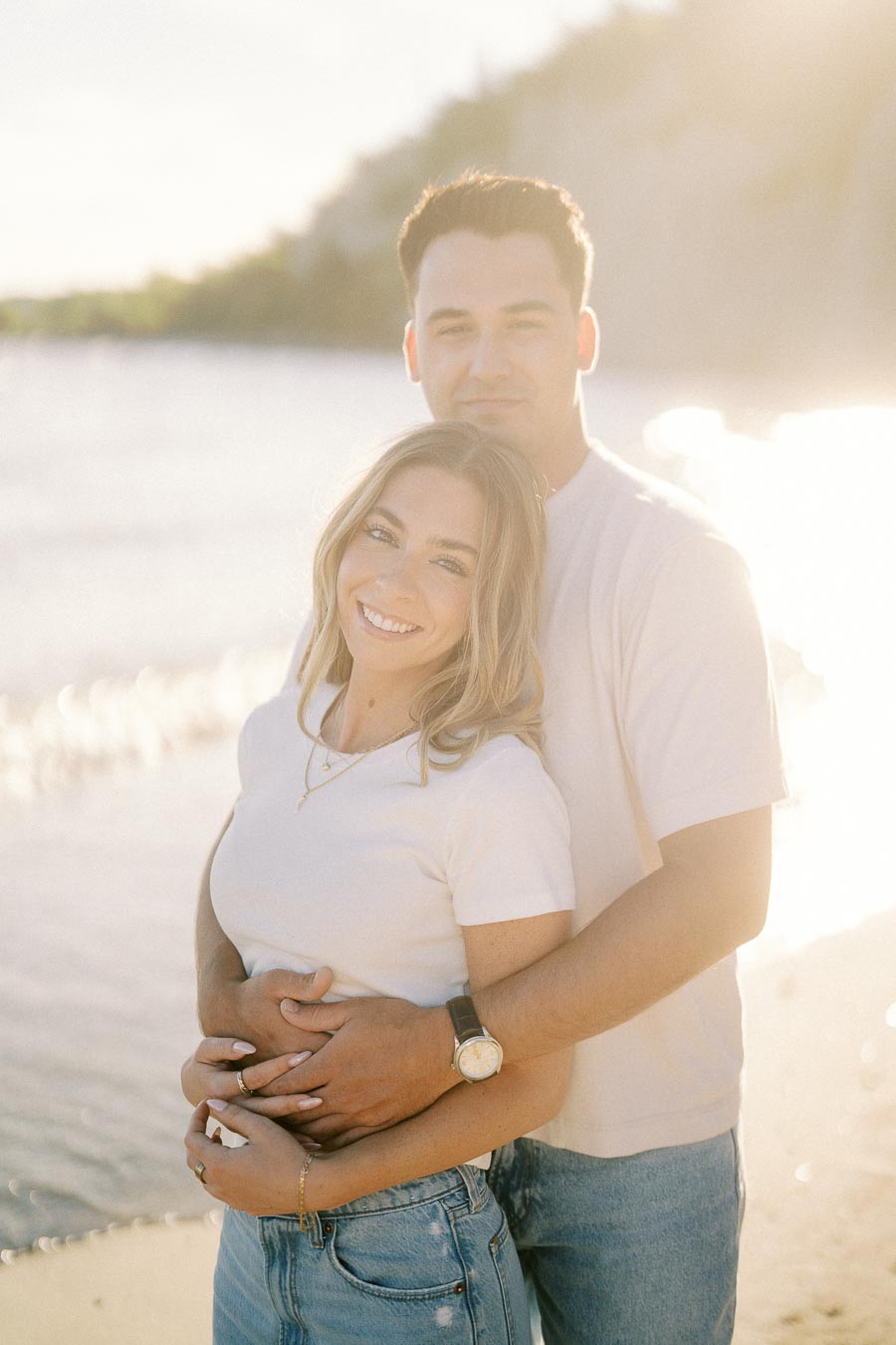Couple smiling and embracing on a sunny beach.