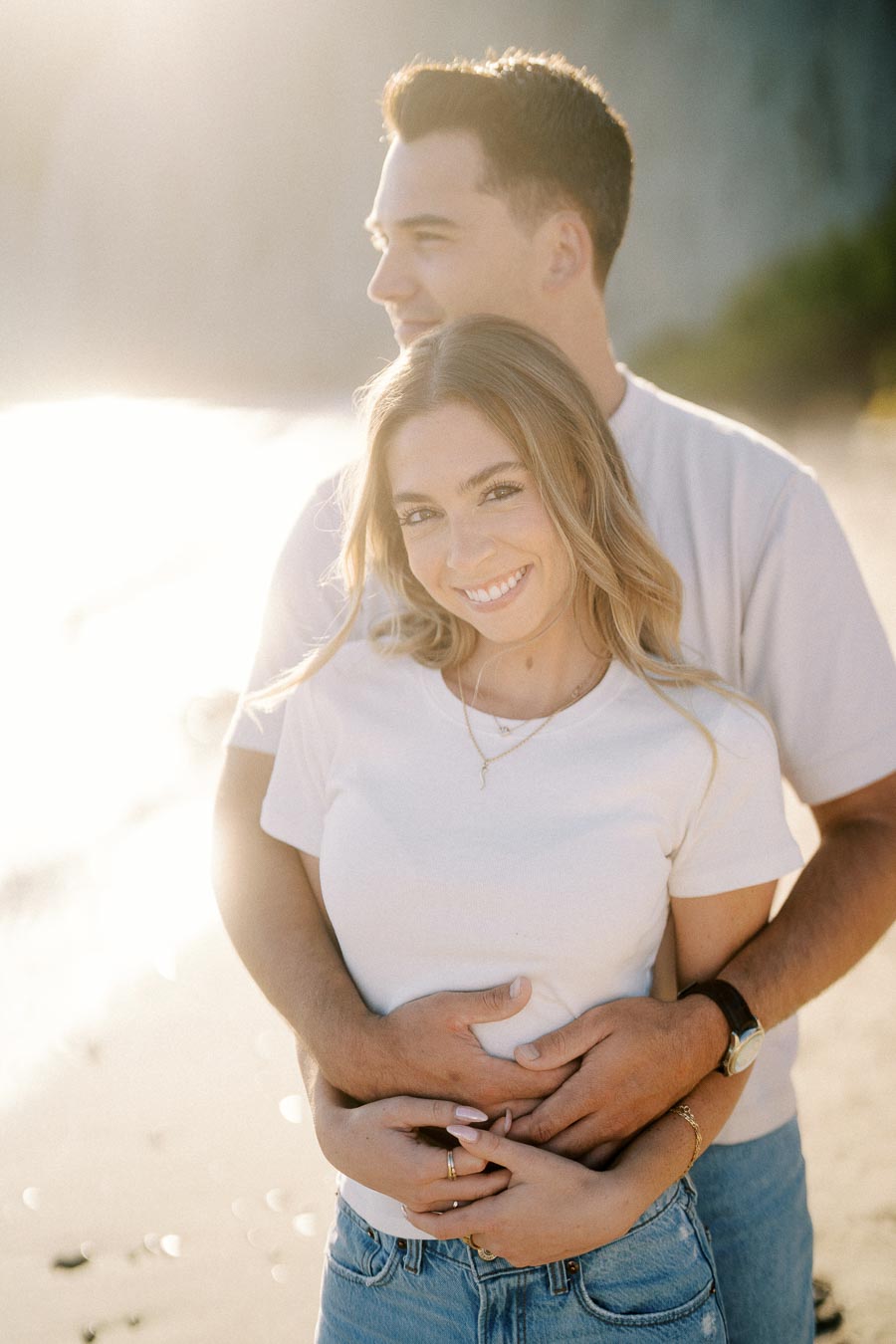 A smiling couple embraces on a sunlit beach, showcasing a warm and romantic moment.