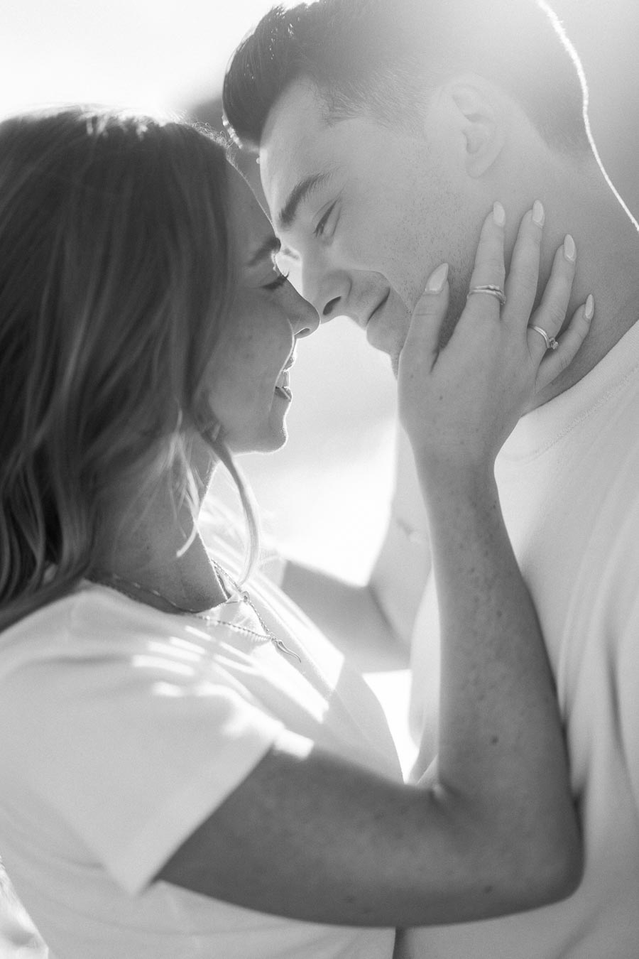 A black-and-white photo of a couple gazing lovingly at each other, with the woman gently touching the man's face, capturing an intimate and romantic moment.