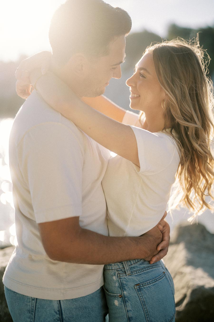 Couple embracing with smiles in natural outdoor lighting near water