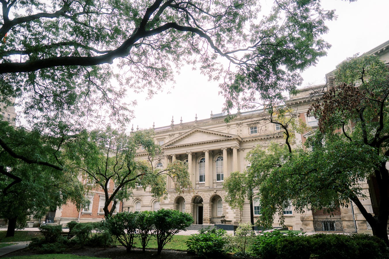 Historic stone building with classical architecture surrounded by lush green trees and foliage.