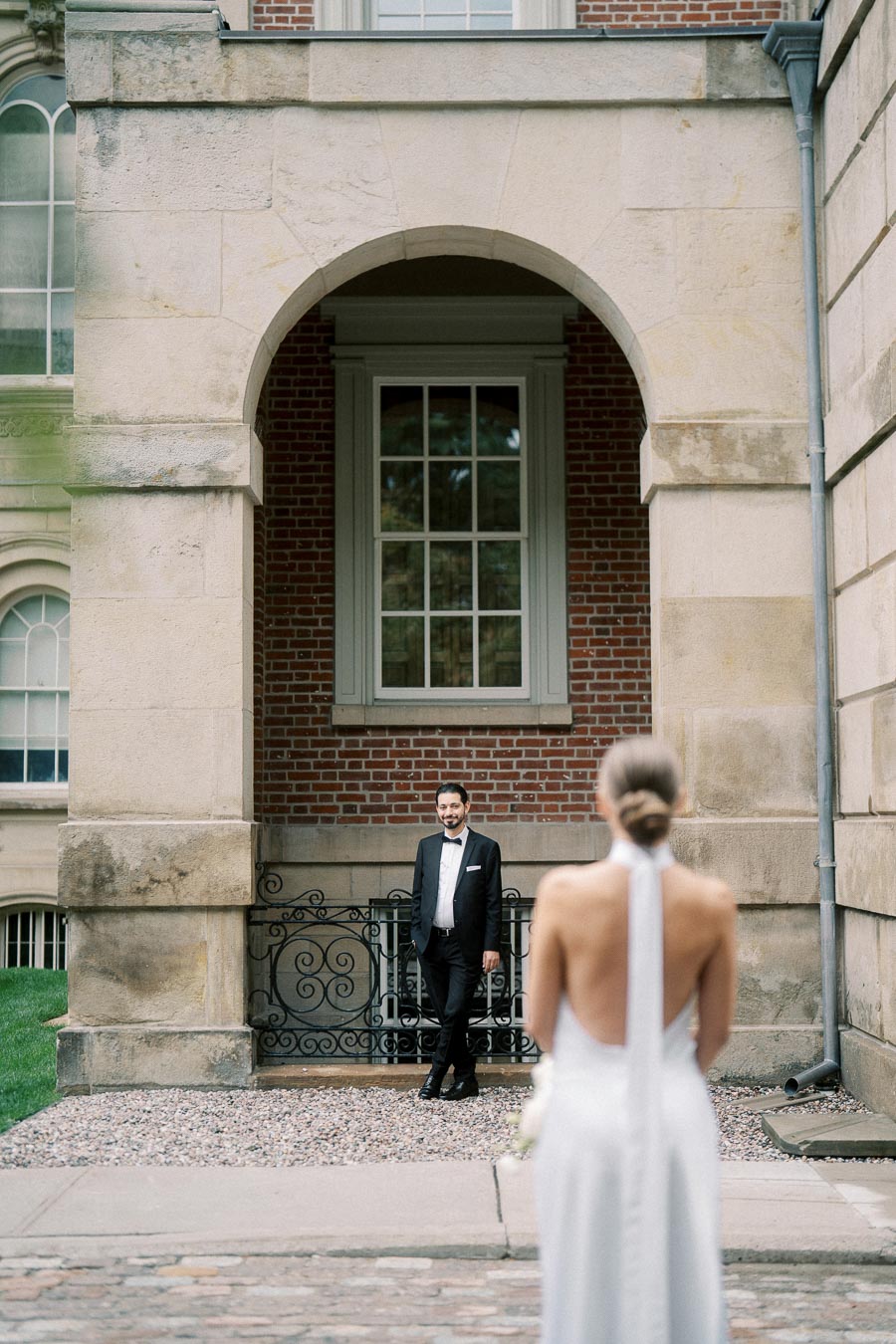 Bride approaching groom for first look in elegant outdoor wedding scene with historic architecture.