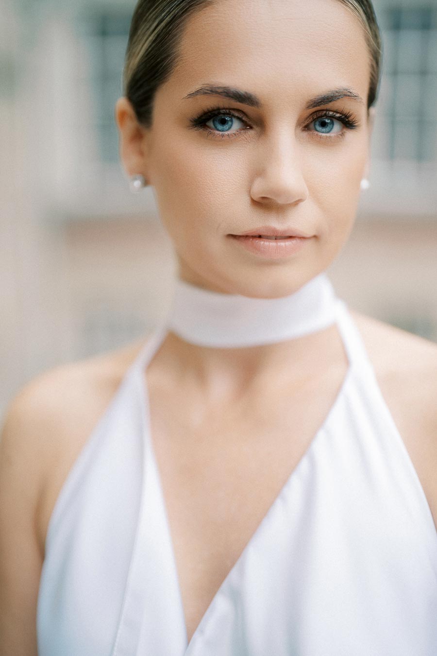 Portrait of a woman with blue eyes and a white halter top in soft natural lighting.